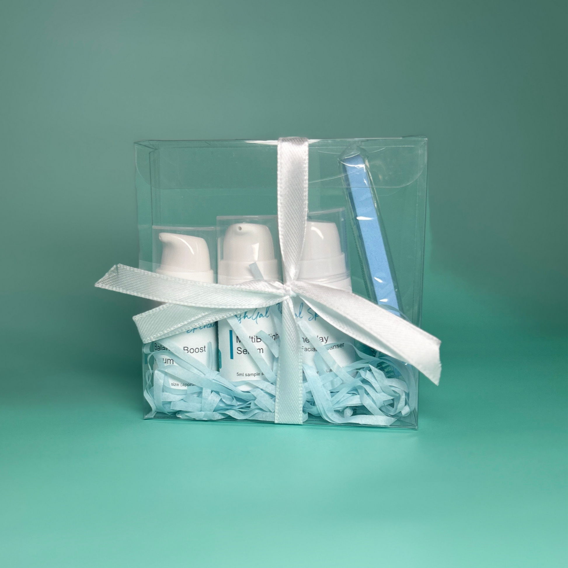 Clear gift box with mini lashgal skincare products and a white ribbon on a teal background